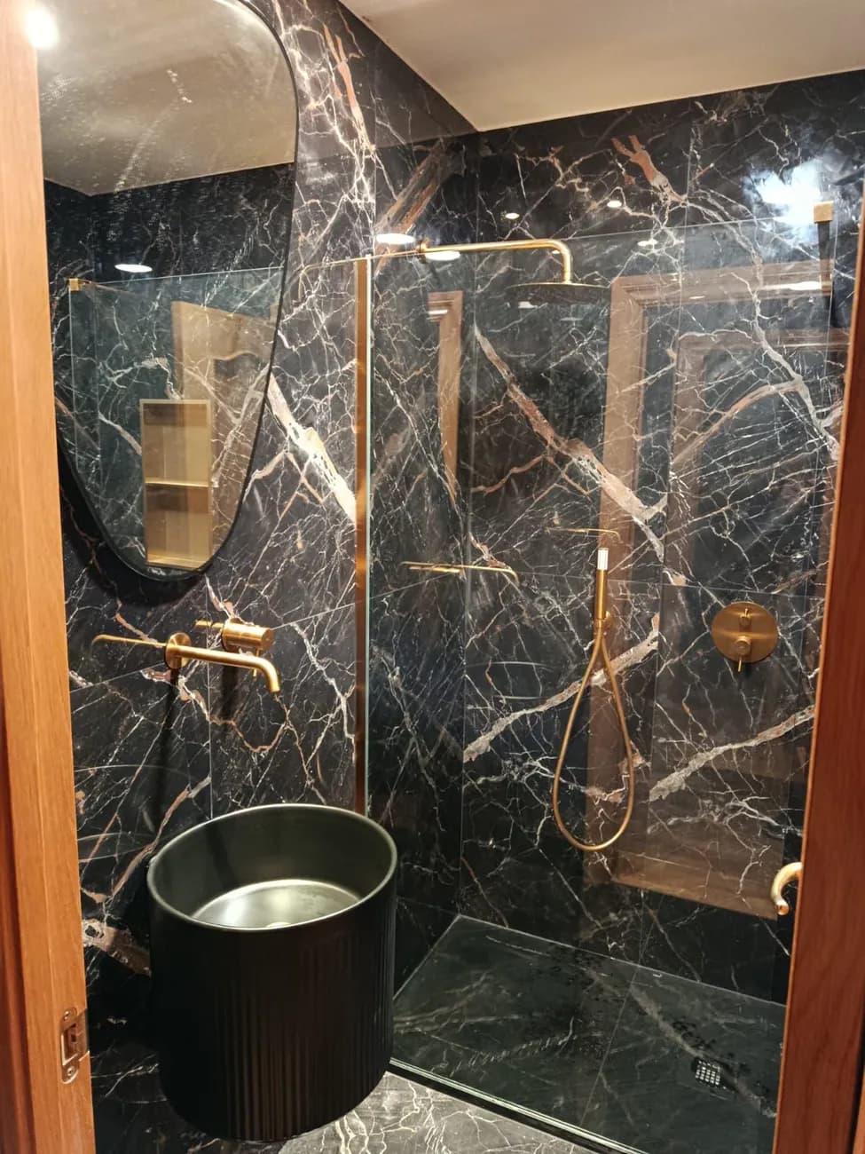Baño de lujo con revestimiento efecto mármol negro y grifería dorada