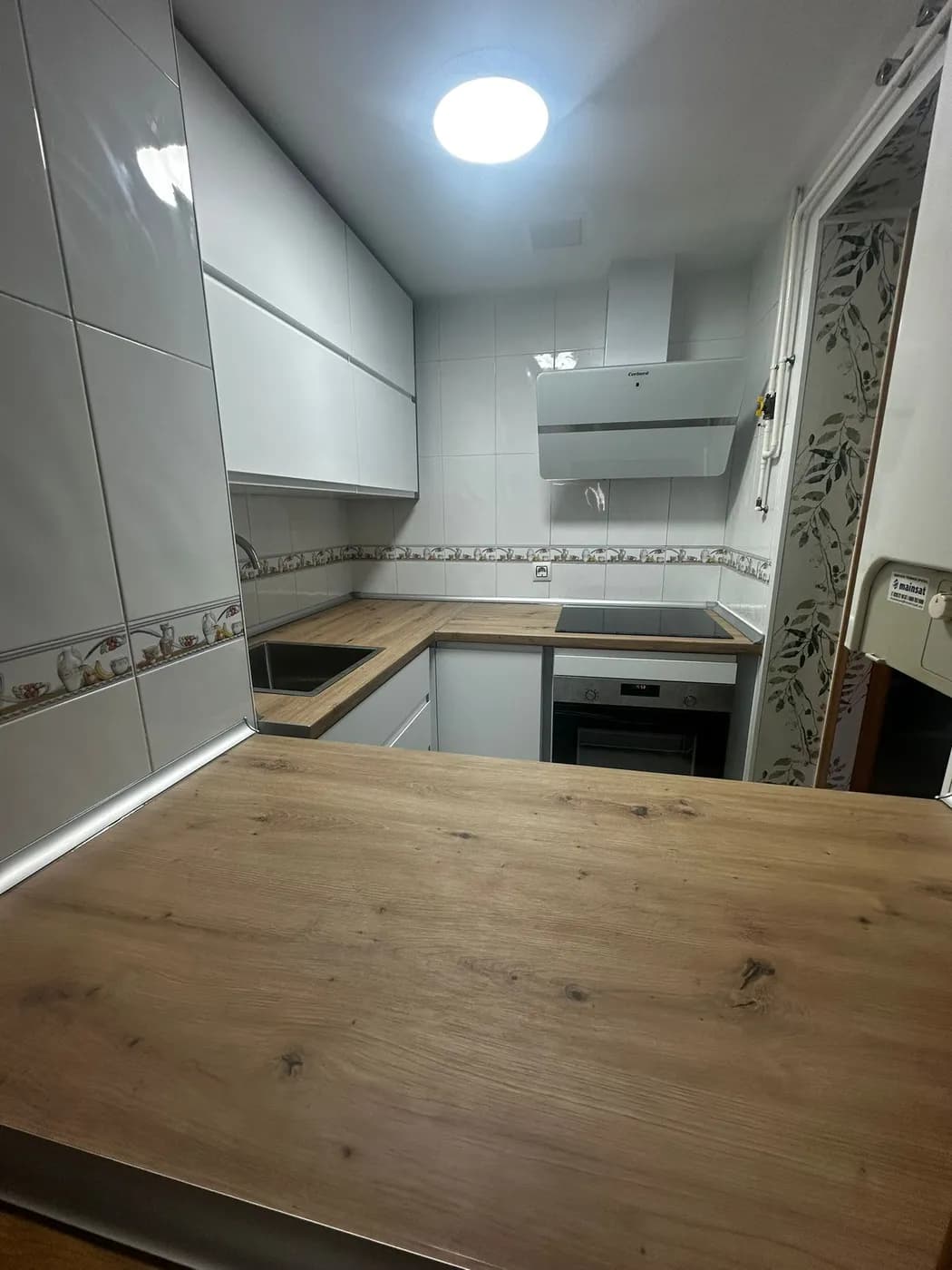 Cocina en L reformada en blanco brillo con encimera de madera